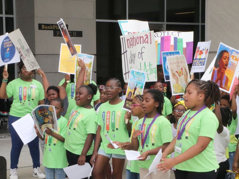 Students in bright green shirts hold signs outside of a building