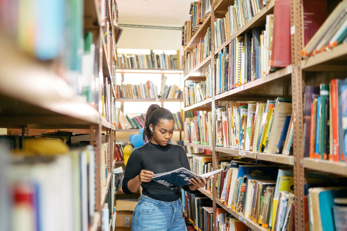A student stands between tall shelves of books, reading