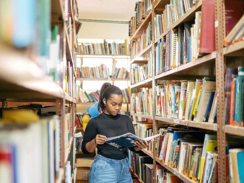 A student stands between tall shelves of books, reading