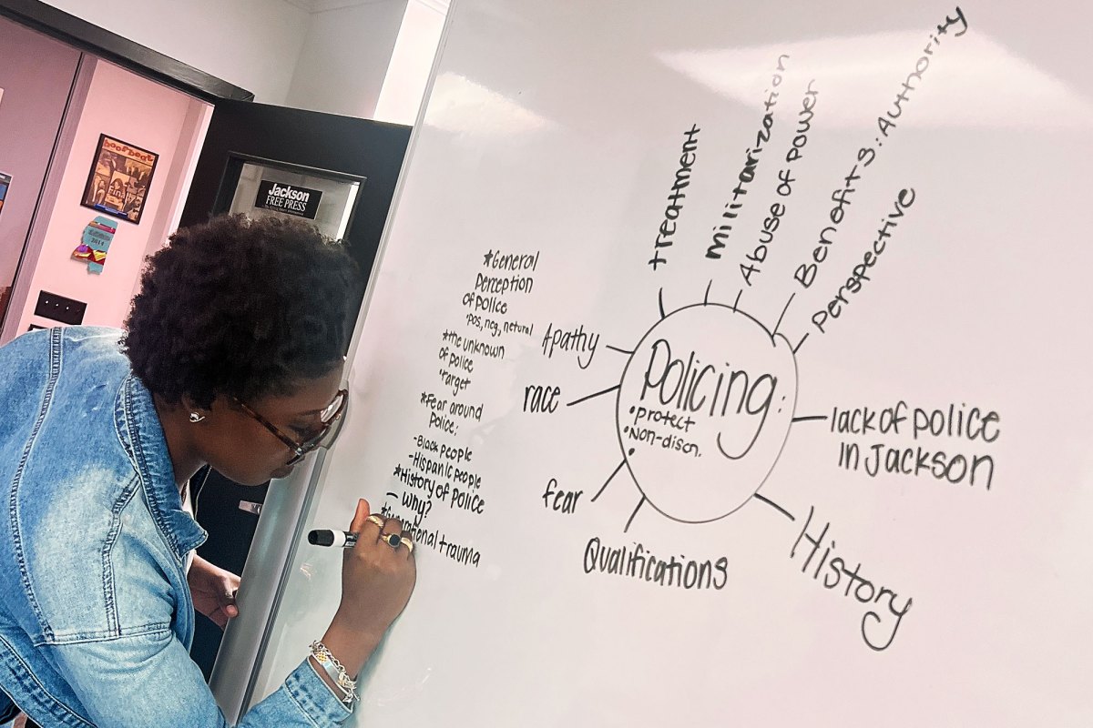 A person writing on a whiteboard, a large word cloud that centers around the word Policing is seen