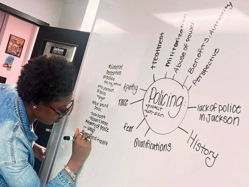 A person writing on a whiteboard, a large word cloud that centers around the word Policing is seen