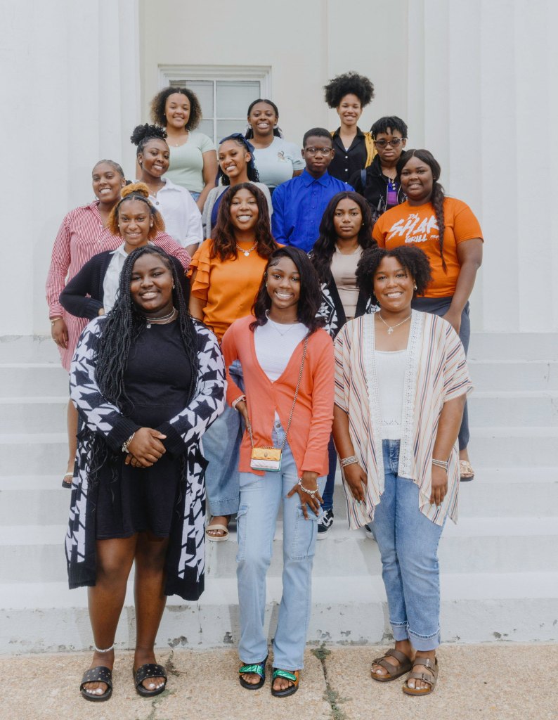 15 teens smile for the camera, posed on white steps