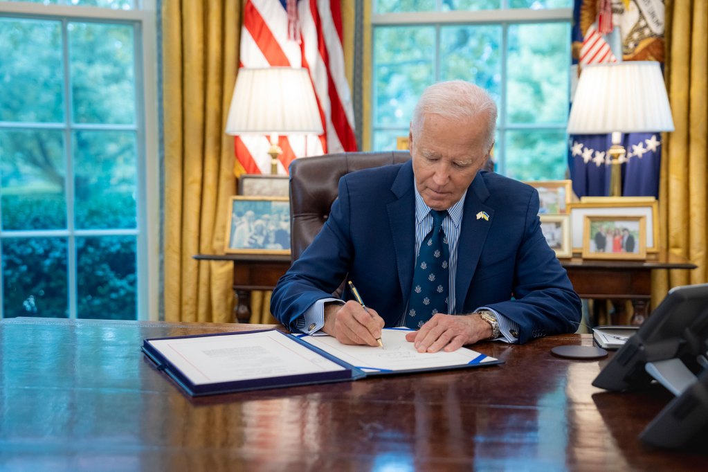 President Biden sits at his desk and signs a document