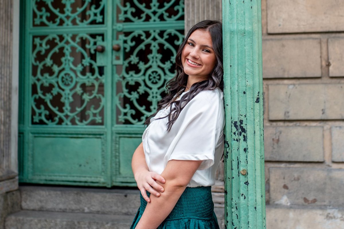 A teen leans against a green pole in front of a green door