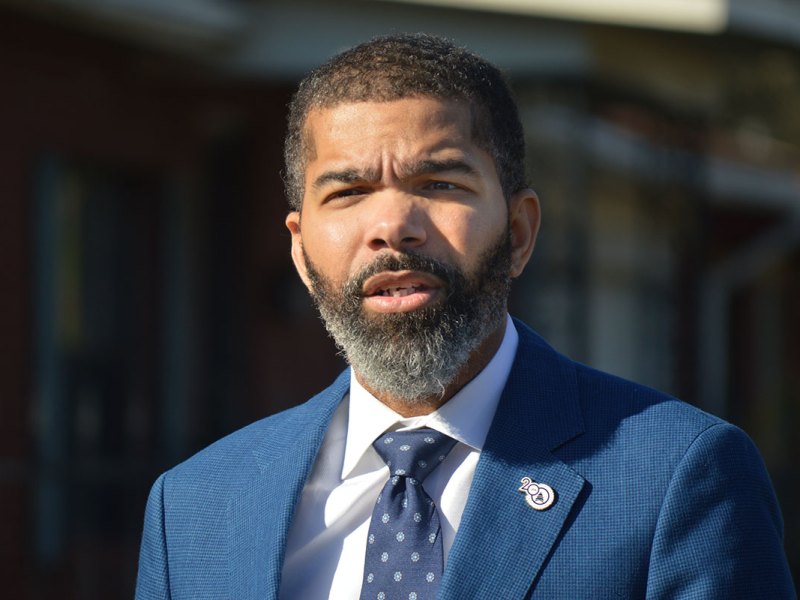 Mayor Chokwe A. Lumumba standing outside in a blue suit and tie. He's standing towards the sunlight and speaking