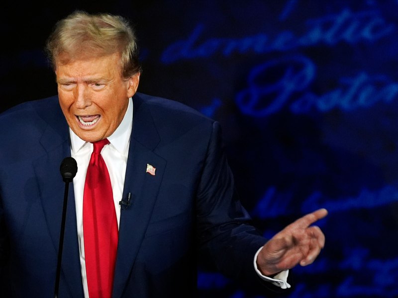 Donald Trump speaking at a mic, hand pointing off to the right