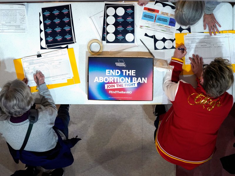 three people lean over a table with a sign that reads End the Abortion Ban, Join the Fight