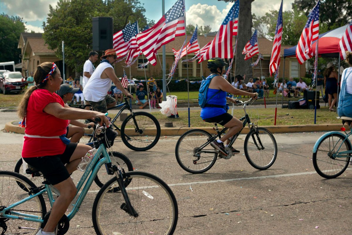Families ride bicyles down the road past a road side decoration of multiple US Flags