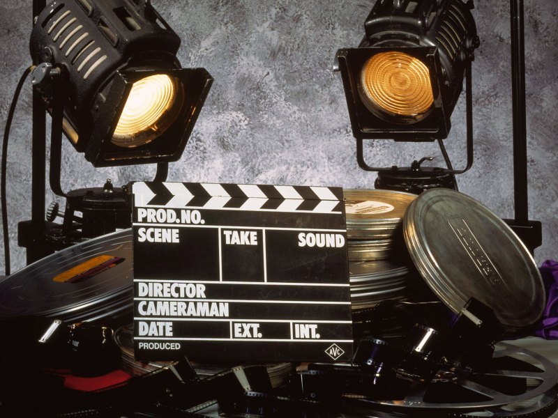 A pile of film reels in and out of cans and a blank film clapboard sit under set lights