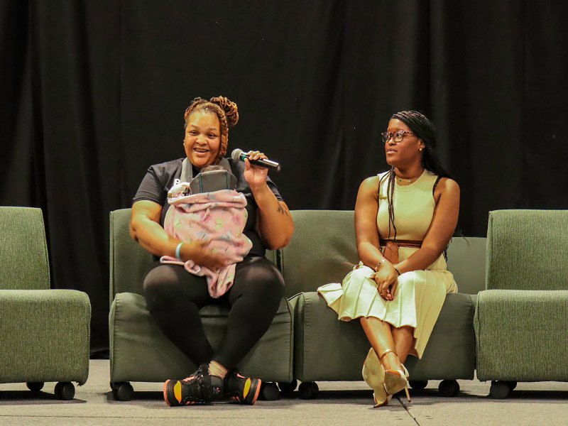 Two women sit on stage and talk