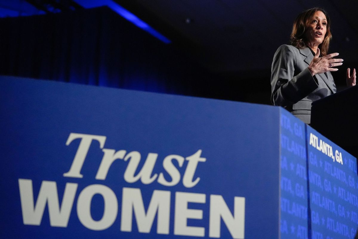 A woman speaks on a stage that is labeled Trust Woman