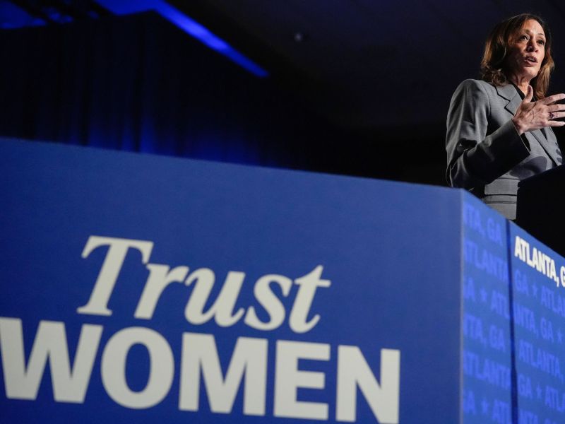 A woman speaks on a stage that is labeled Trust Woman