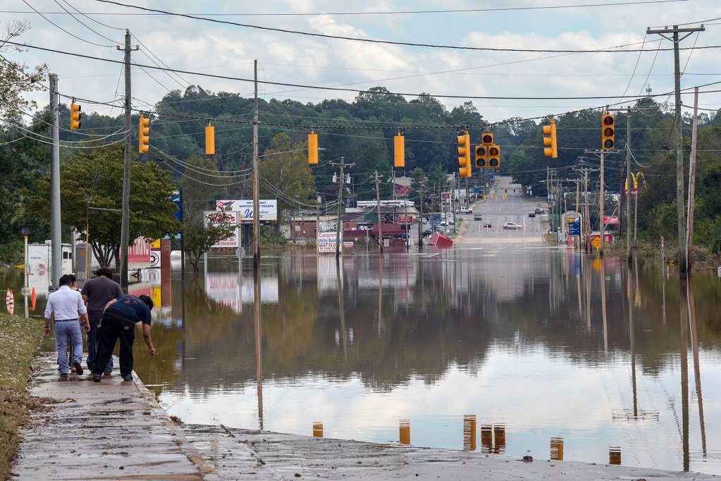 Yellow street lights hang over a flooded road as people walk up to the edge of the water