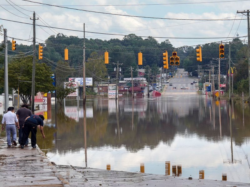 Yellow street lights hang over a flooded road as people walk up to the edge of the water
