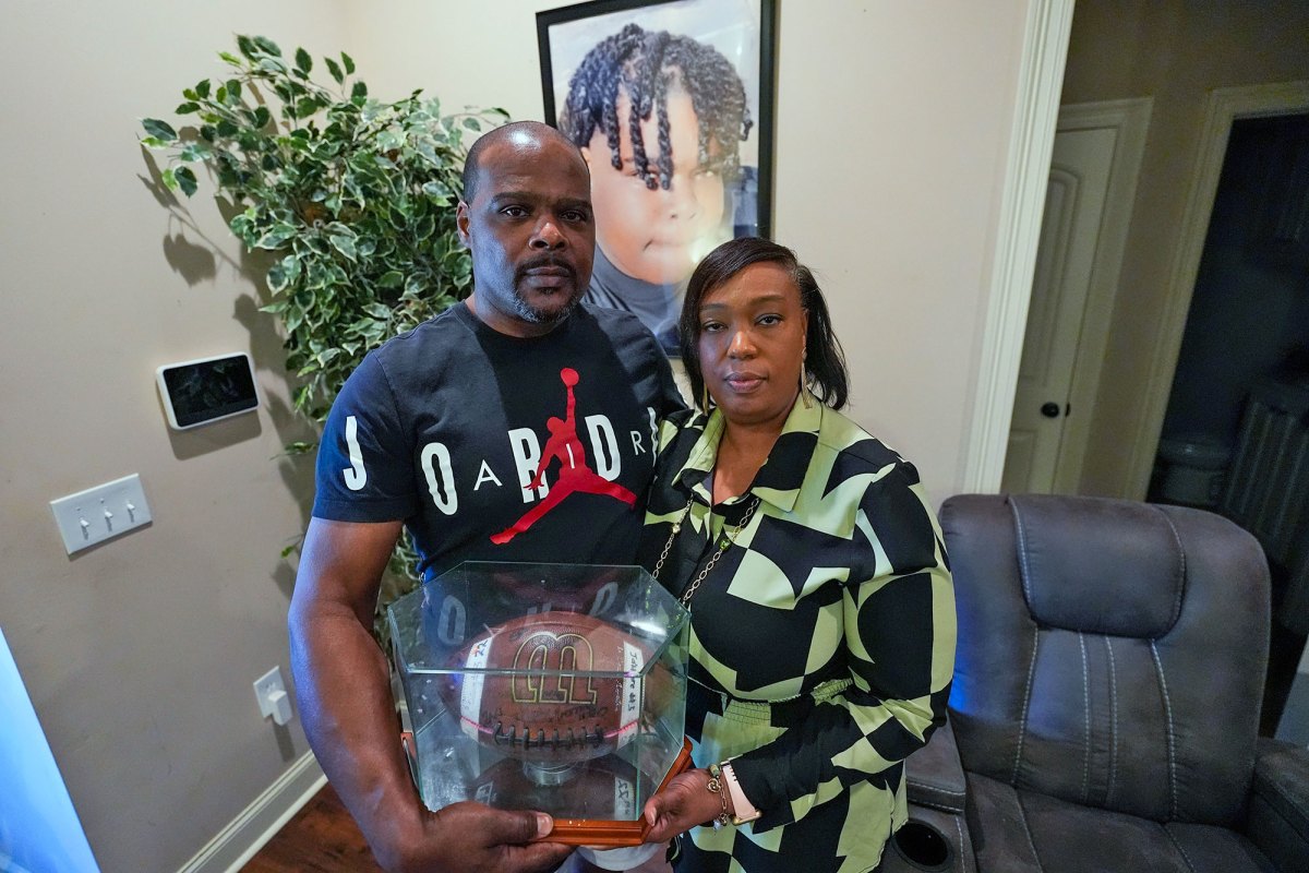 Phillip Laster Sr. and his wife Ashanta Laster stand in their living room and hold a football signed by teammates of their son Phillip Laster Jr.