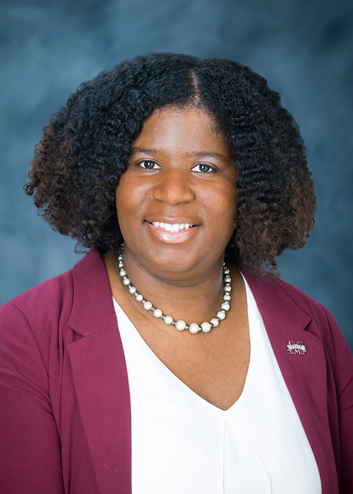 An official portrait of a woman with shoulder length hair, a burgundy jacket and white necklace