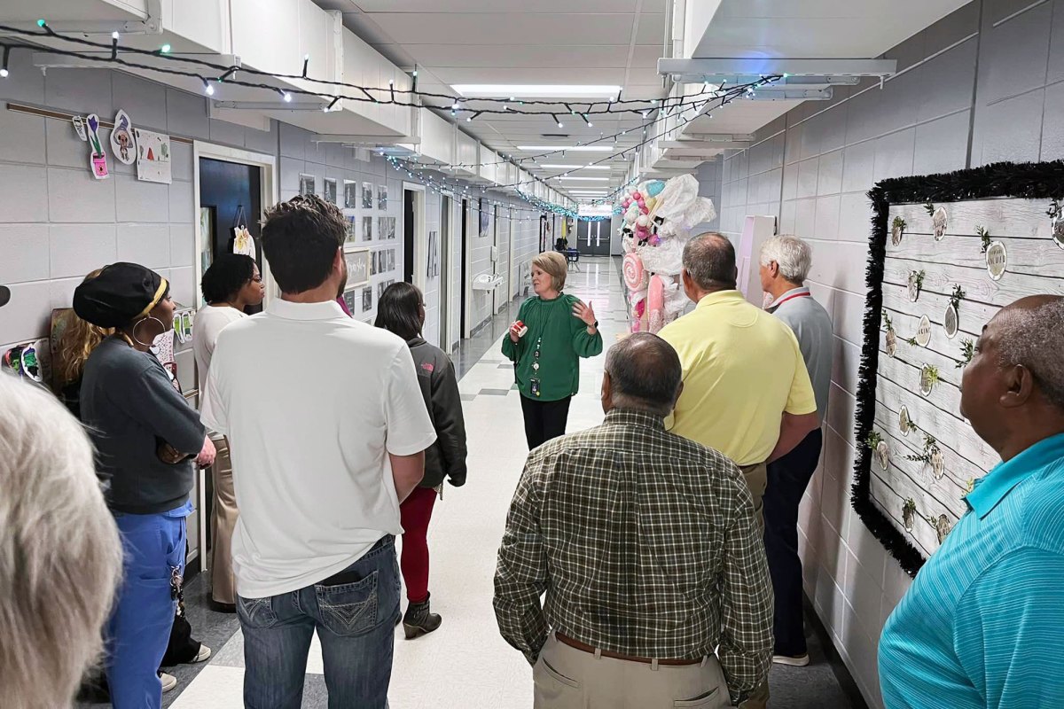 A school hallway full of adults follow a woman in a green top as she guides them