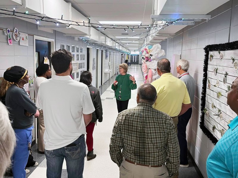 A school hallway full of adults follow a woman in a green top as she guides them
