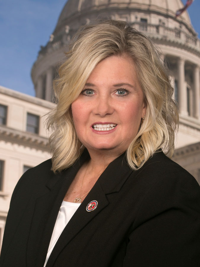 A blonde woman in a black suit poses before the Mississippi state capitol building