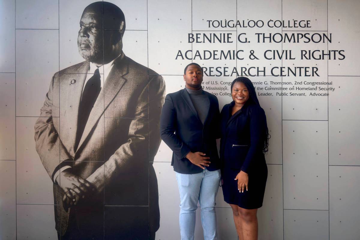 A man and a woman pose together under a sign that reads Tougaloo College Bennie G. Thompson Academic & Civil Rights Research Center