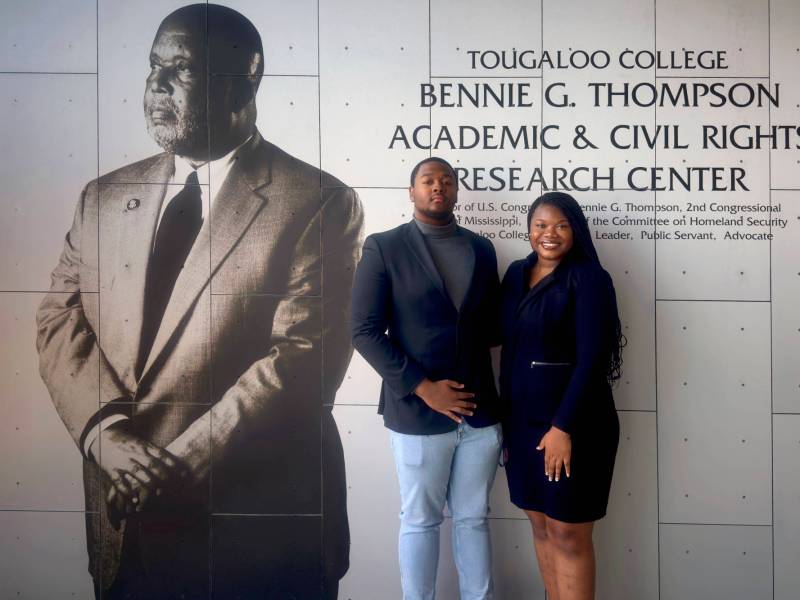 A man and a woman pose together under a sign that reads Tougaloo College Bennie G. Thompson Academic & Civil Rights Research Center