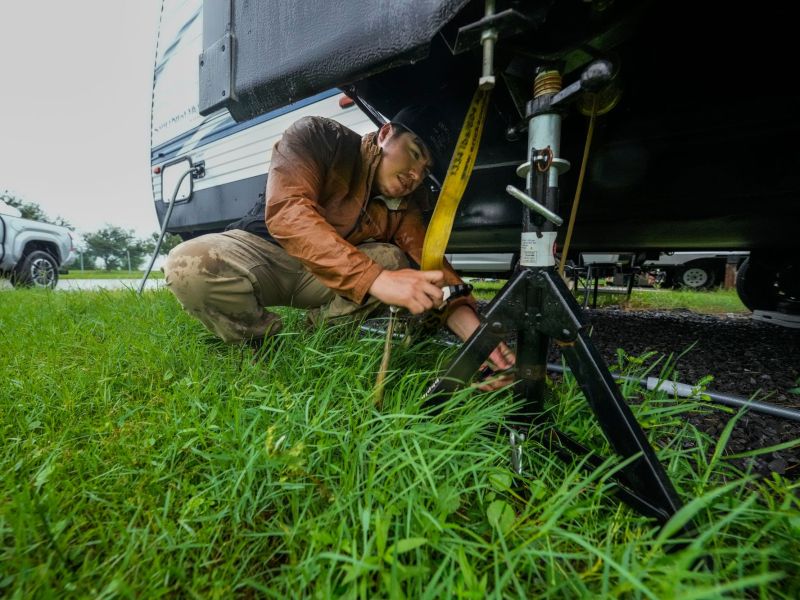 A man is seen using a jack support on his mobile trailer