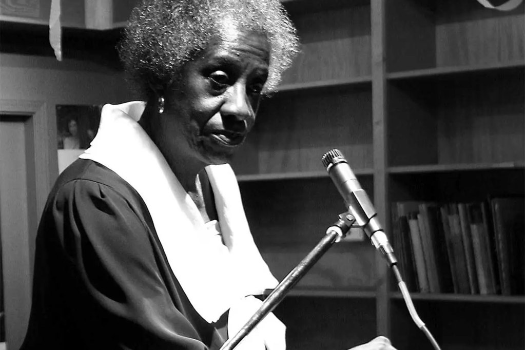 A black and white photo of an older woman sitting before a mic
