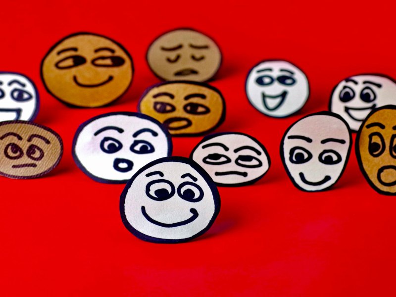 Stick figure style faces drawn and cut out, resting on a red background