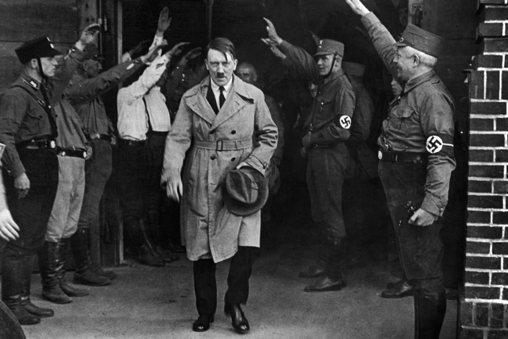 Adolph Hitler leaving a building, surrounded by uniformed men giving the Nazi salute