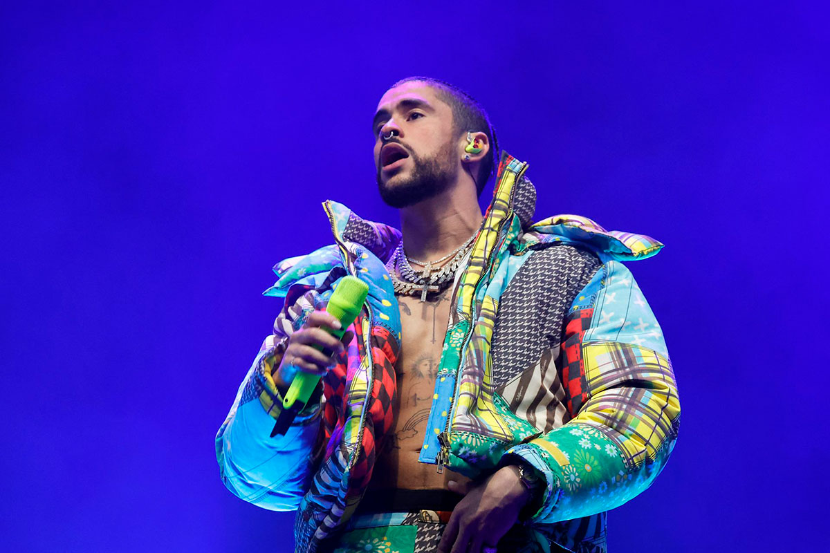 A singer in a multicolored jacket holds a bright green mic on a blue stage