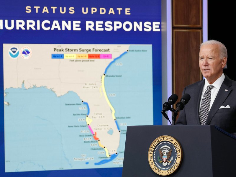 President Biden stands in front of a screen that reads Status Update Hurricane Response and shows a weather map of Florida