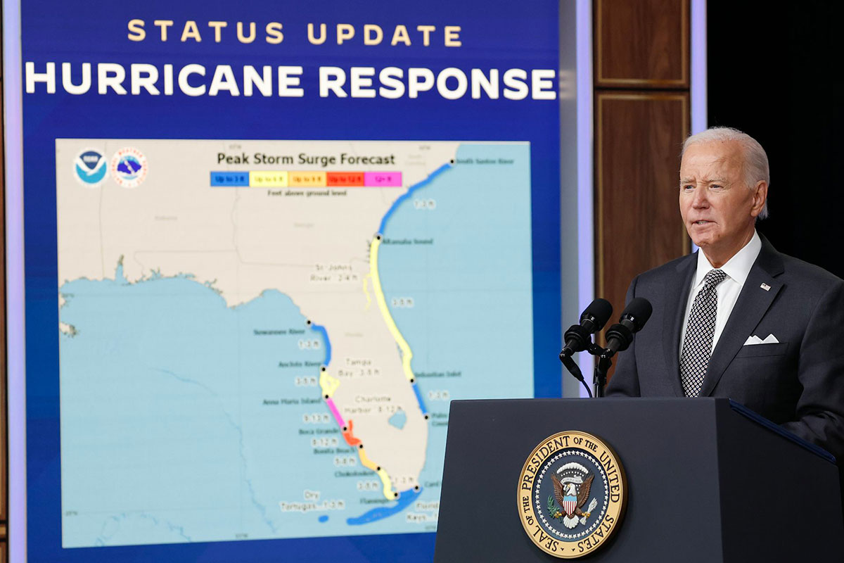 President Biden stands in front of a screen that reads Status Update Hurricane Response and shows a weather map of Florida