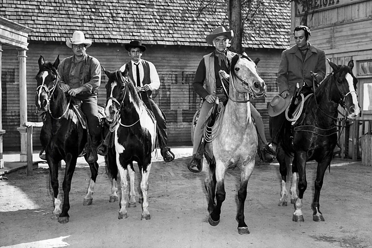 Four members of the cast of Bonanza seem riding horses through town