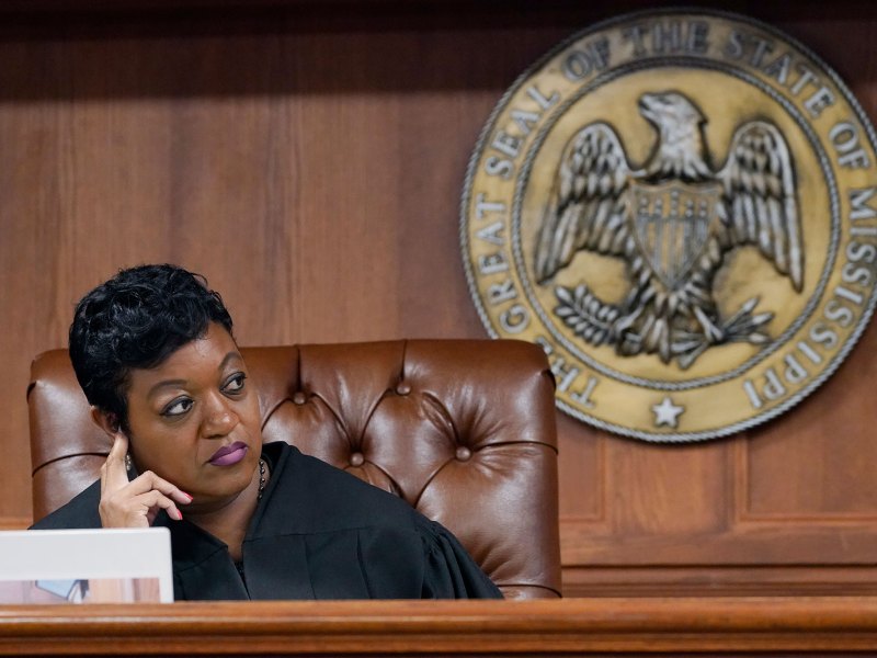A judge sits at her desk. The Seal of the State of Mississippi hangs behind the chair.