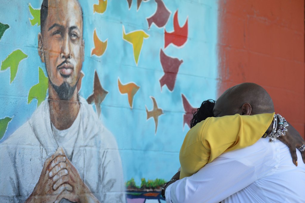 Two people hug outside in front of a painted mural