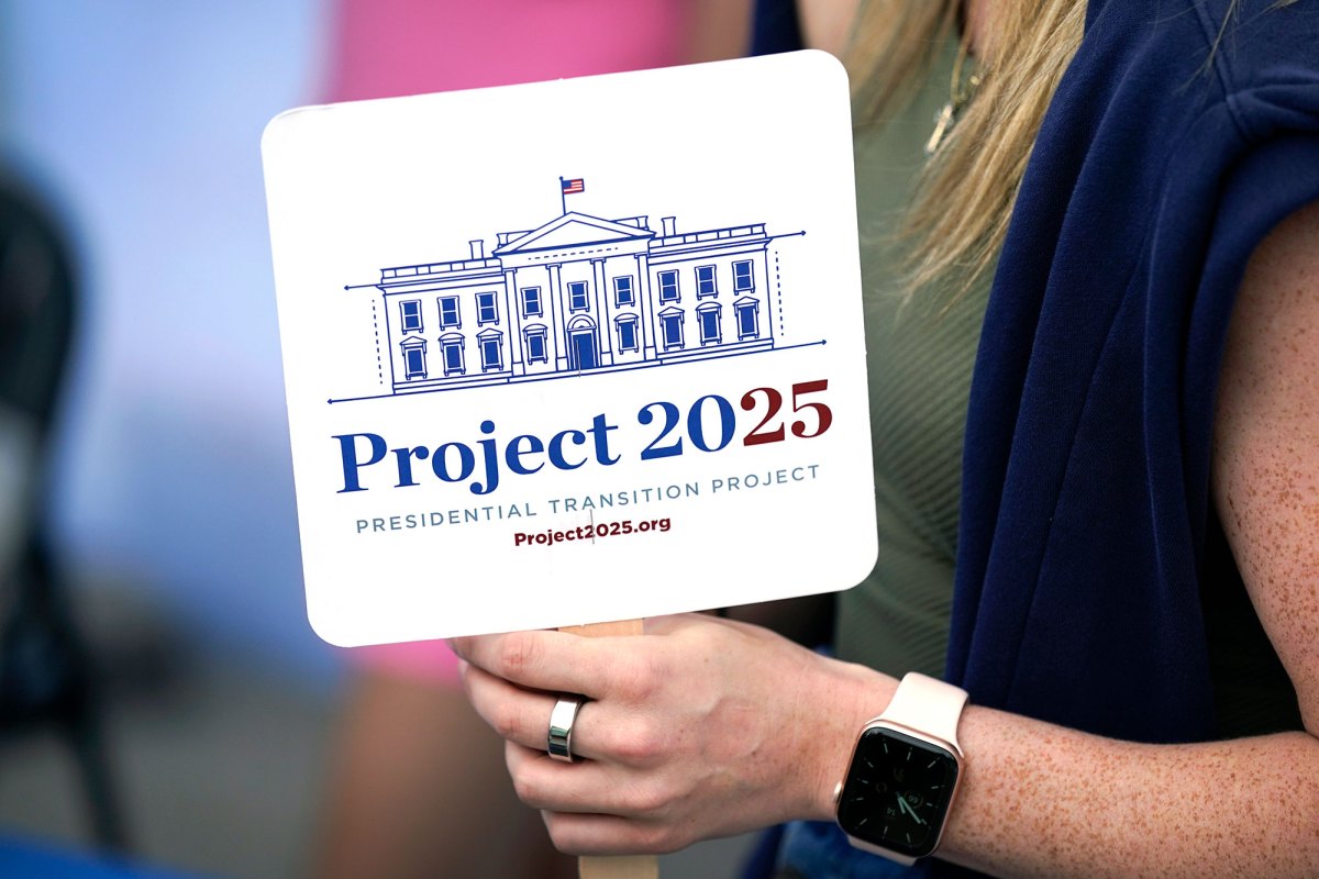 A closeup of a fan that reads "Project 2025" held by a woman's hand