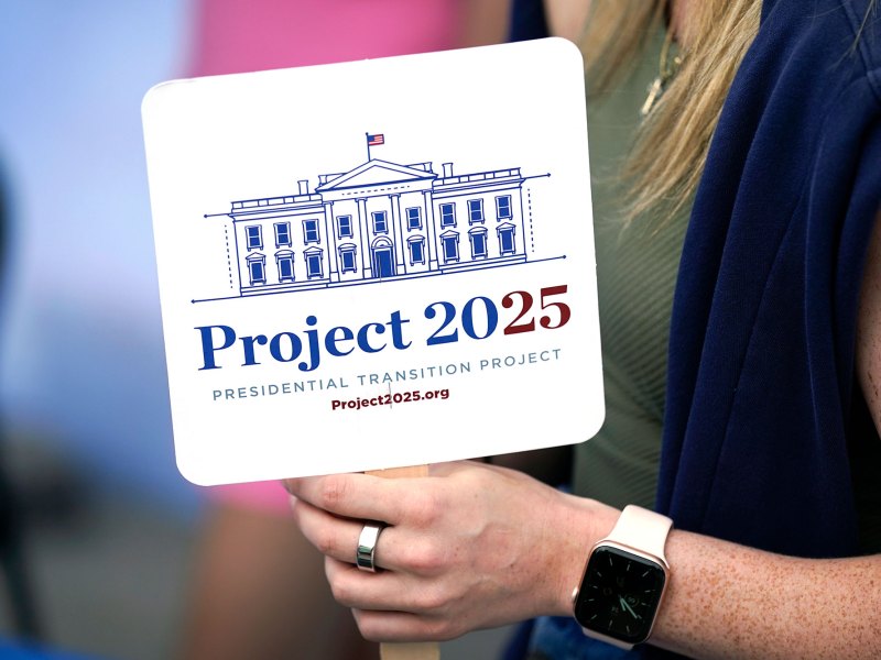 A closeup of a fan that reads "Project 2025" held by a woman's hand