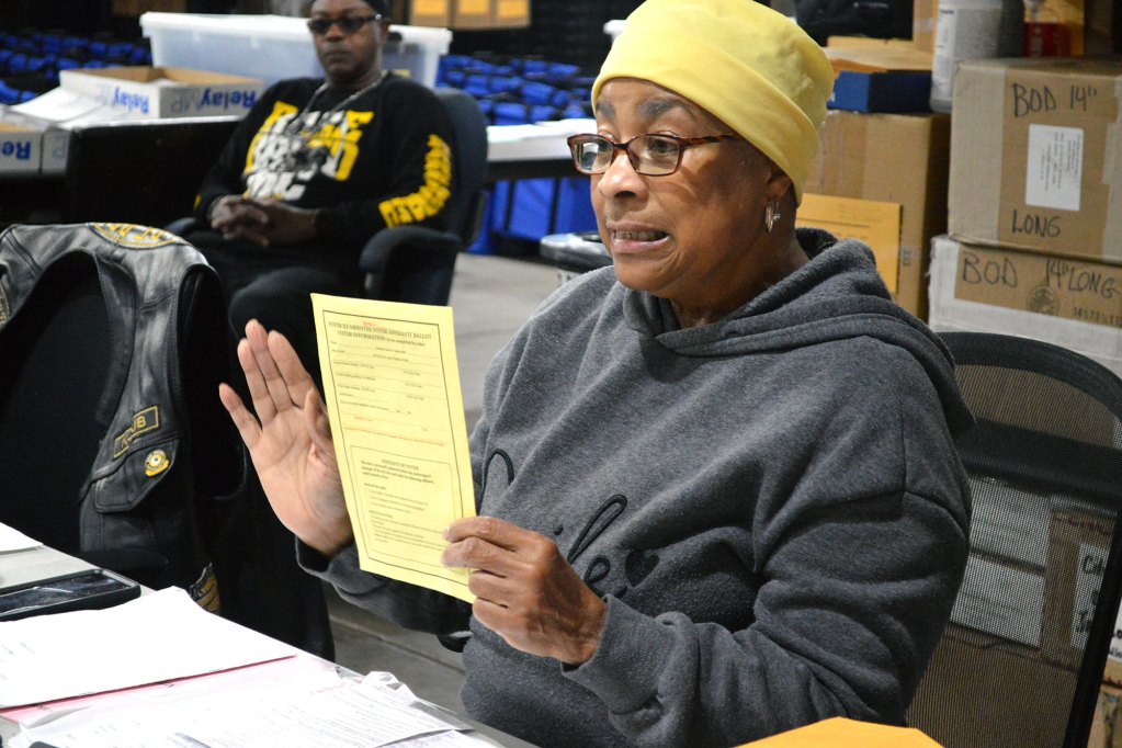 A woman in a yellow hat holds up a yellow piece of paper