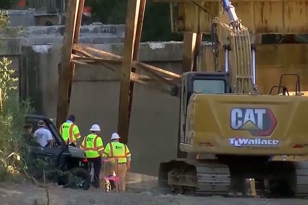 a screenshot shows construction workers and a CAT tractor at the site of a collapsed bridge