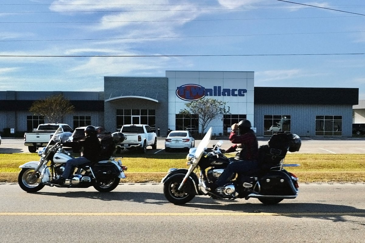 Two motorcyclists drive past a T.L. Wallace building