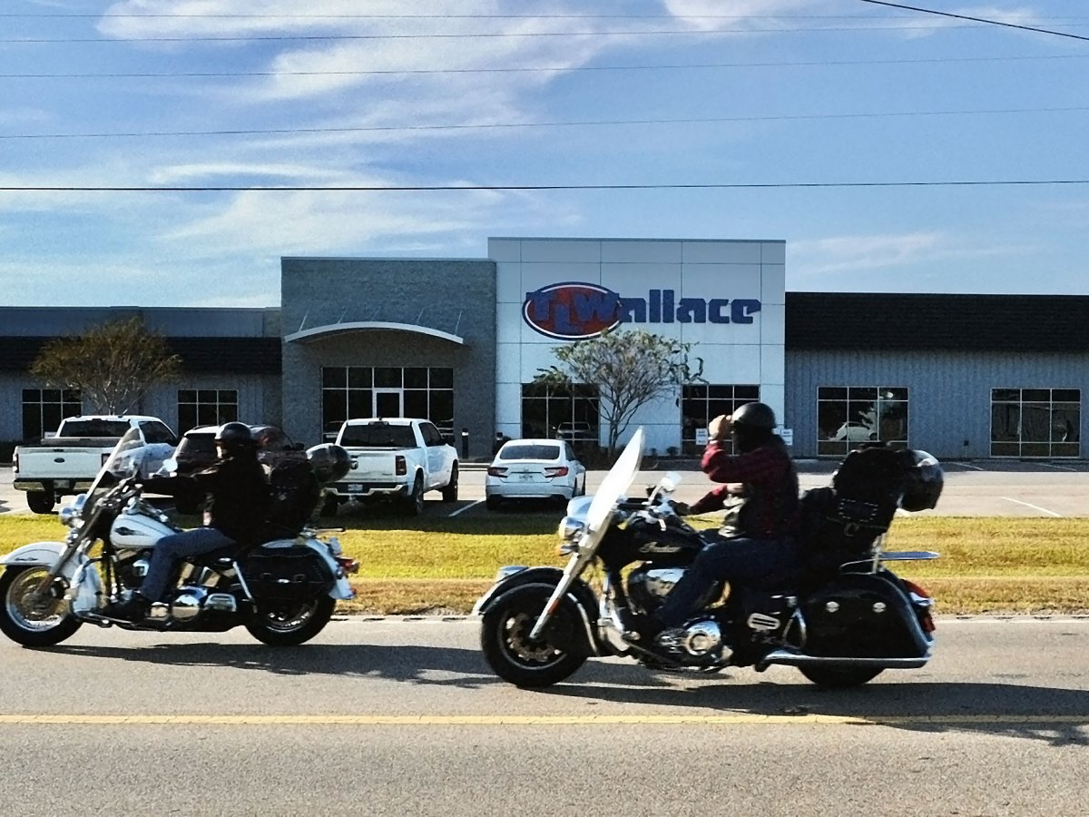 Two motorcyclists drive past a T.L. Wallace building