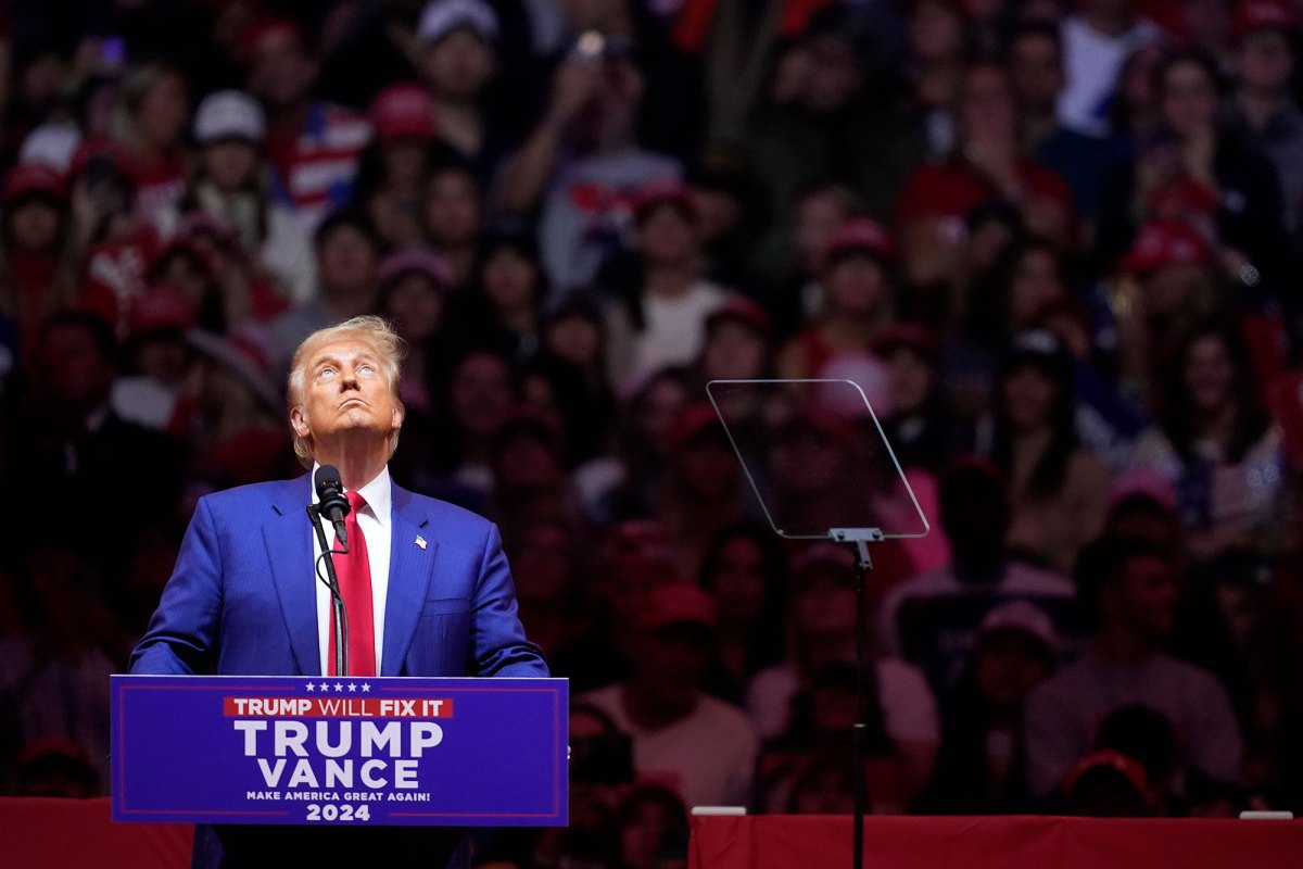 Donald Trump standing at a Trump/Vance podium with a large crowd visible behind him