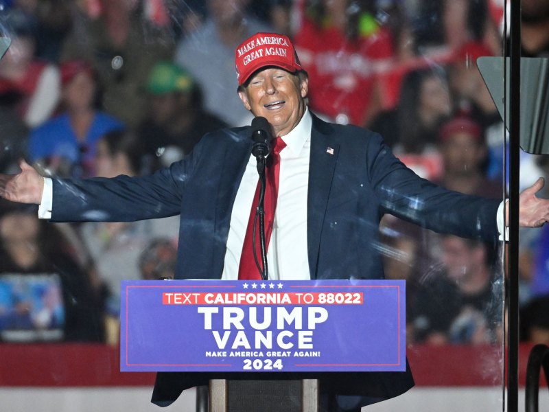 Donald Trump stands in front of a rally with arms out wide