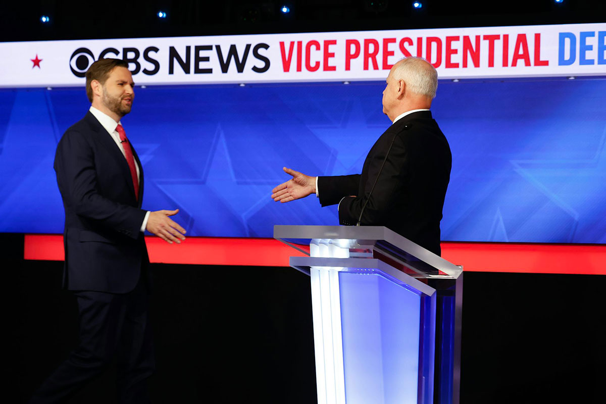 Two men go to shake hands behind a podium. A sign above them reads CBS News Vice Presidential Debate