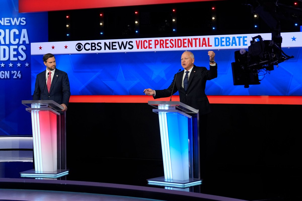 Two men stand at podiums for a Vice Presidential debate. One is lit red and one is lit blue.