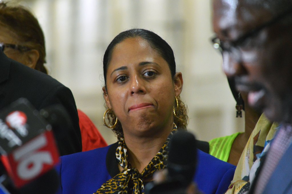 A woman looks on as a man speaks at a press conference