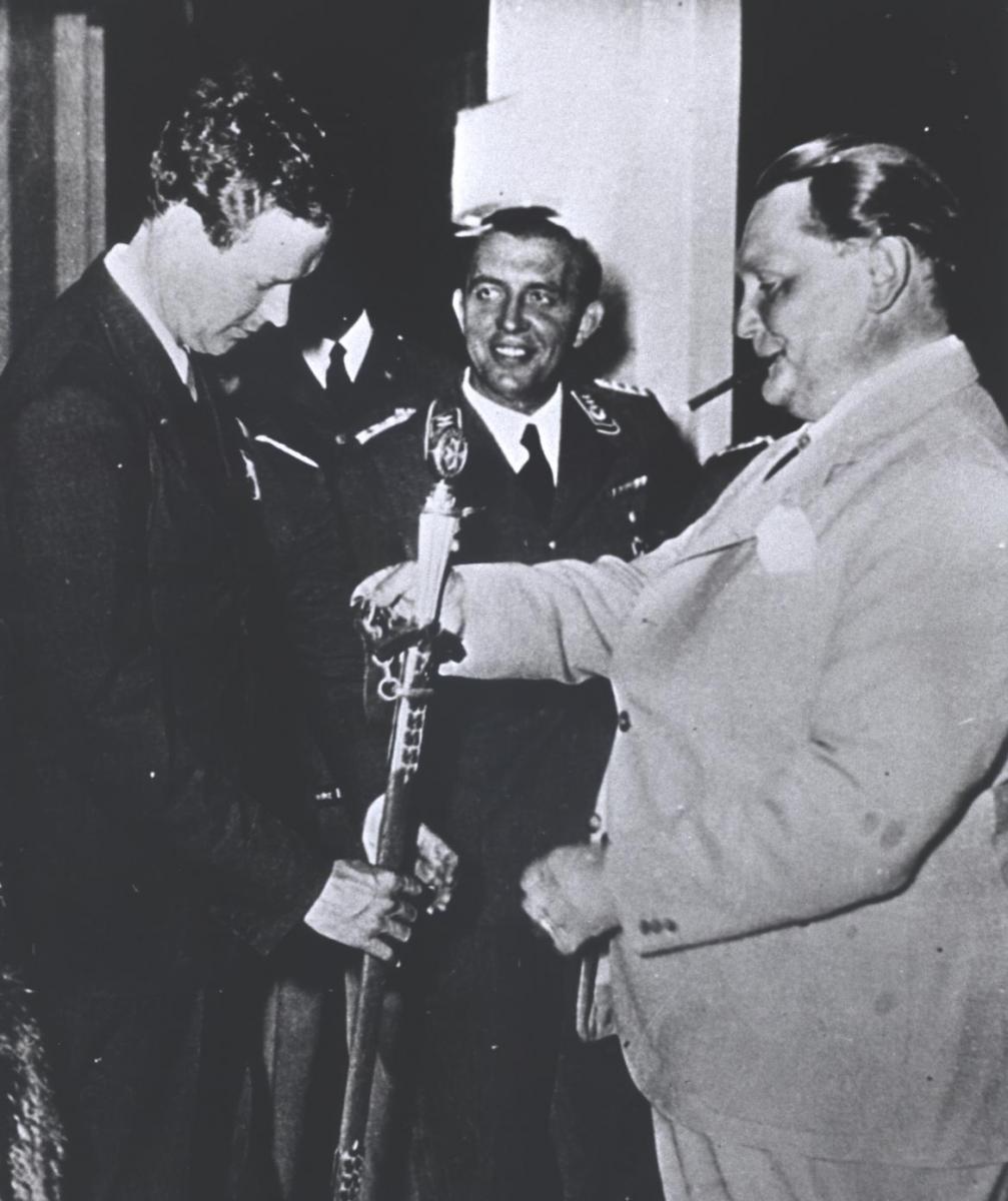 white man with head bowed as he accepted medal from heavy white man smoking a cigar