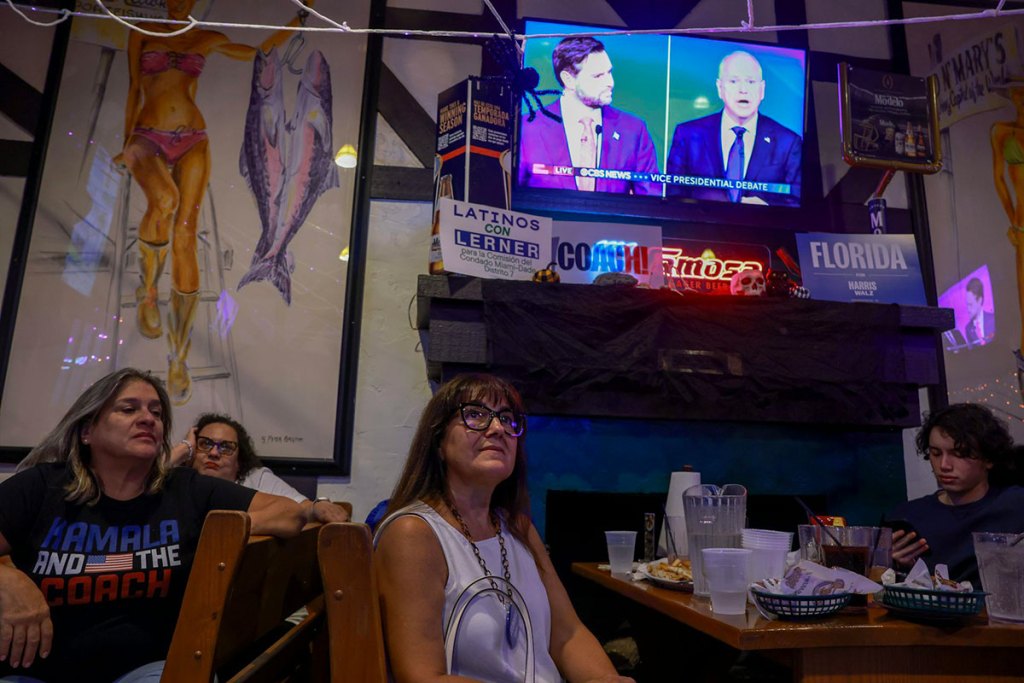 People at a restaurant watching a video screen up high on a wall.