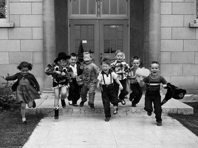Several kids in Halloween costumes are seen running from the school doors excitedly