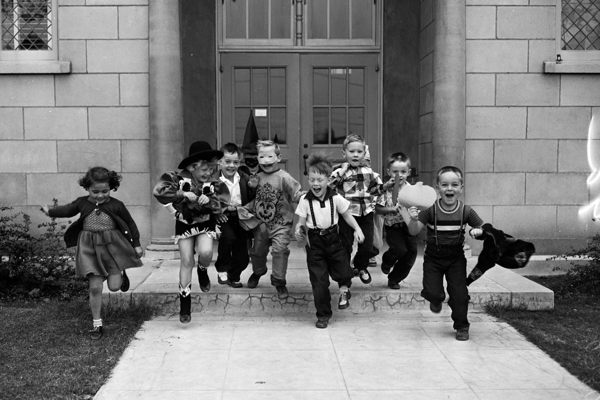 Several kids in Halloween costumes are seen running from the school doors excitedly